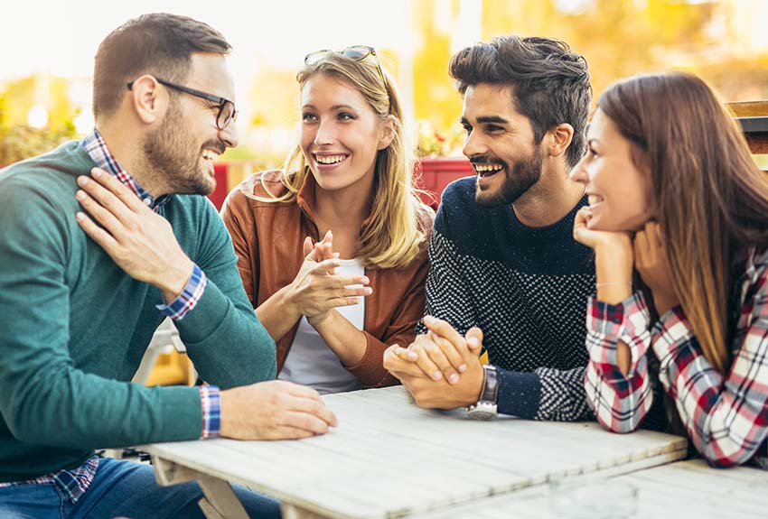Four young people sitting around a sidewalk cafe table having a conversation
