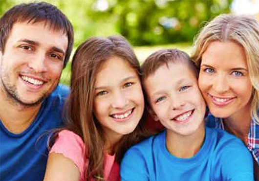Happy Family, husband, wife and two preteen kids smiling for a portrait while outside at a park