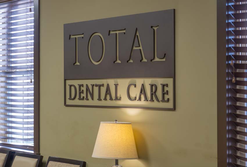 Total Dental Care metal signage hanging on the lobby wall above a lamp