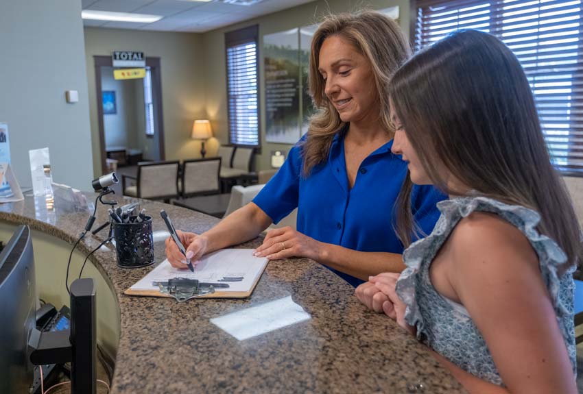 Mother and Daughter sign paperwork standing at the front counter in the lobby of Total Dental