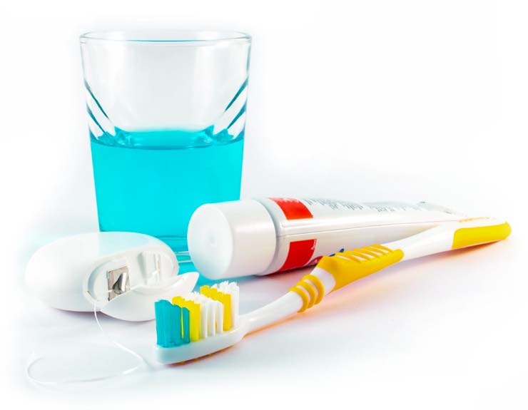 close-up photo of a glass with mouthwash, a tube of toothpaste, a container of dental floss and a tooth brush laid out on a bathroom counter