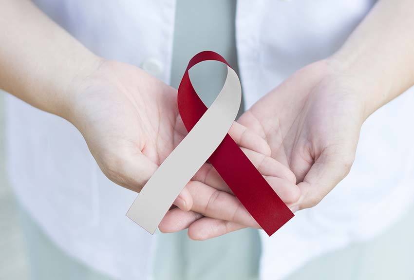 hands holding a red and beige oral cancer cancer ribbon