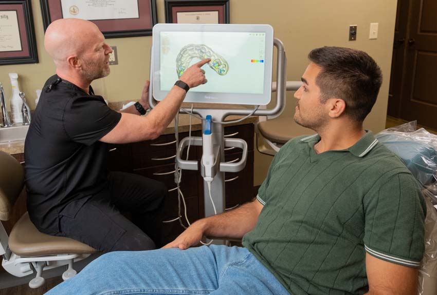 Dr. Harper with a middle aged male patient looking at a computer screen of a 3-D scan showing teeth.