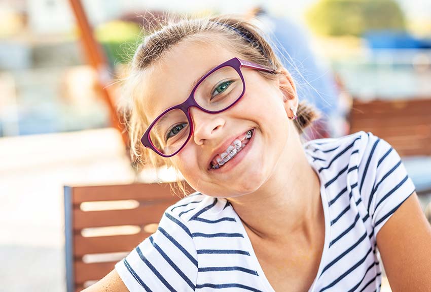 Young girl with glasses smiling showing her braces