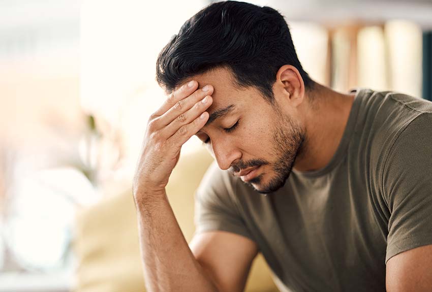 Young man sitting in a room, holding his head in pain